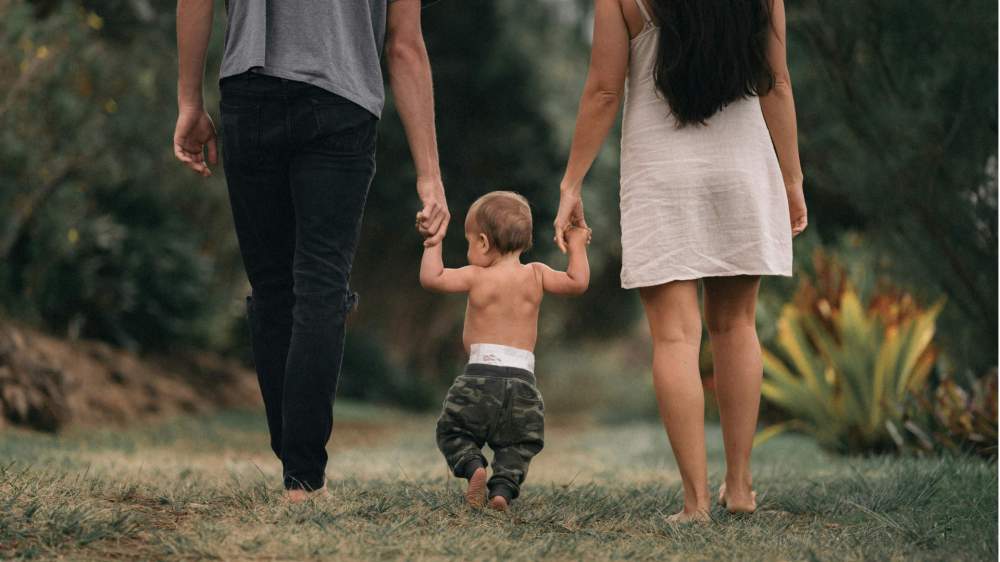 baby walking between parents